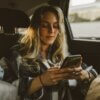 young caucasian woman using facebook instagram ads smartphone sitting in backseat of car