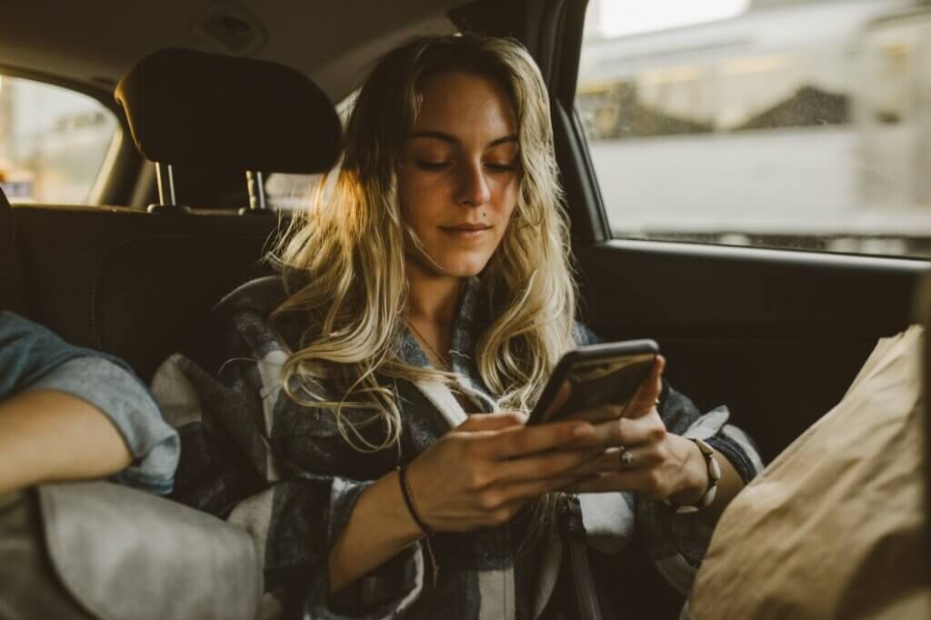 young caucasian woman using facebook instagram ads smartphone sitting in backseat of car