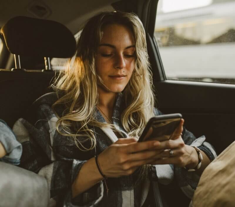 young caucasian woman using facebook instagram ads smartphone sitting in backseat of car